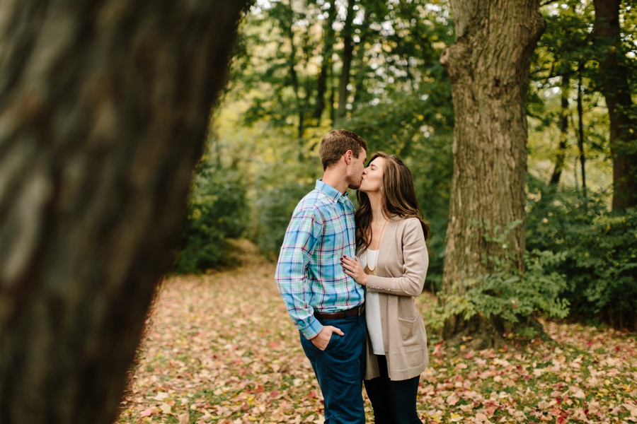 Engaged couple kissing under fall trees