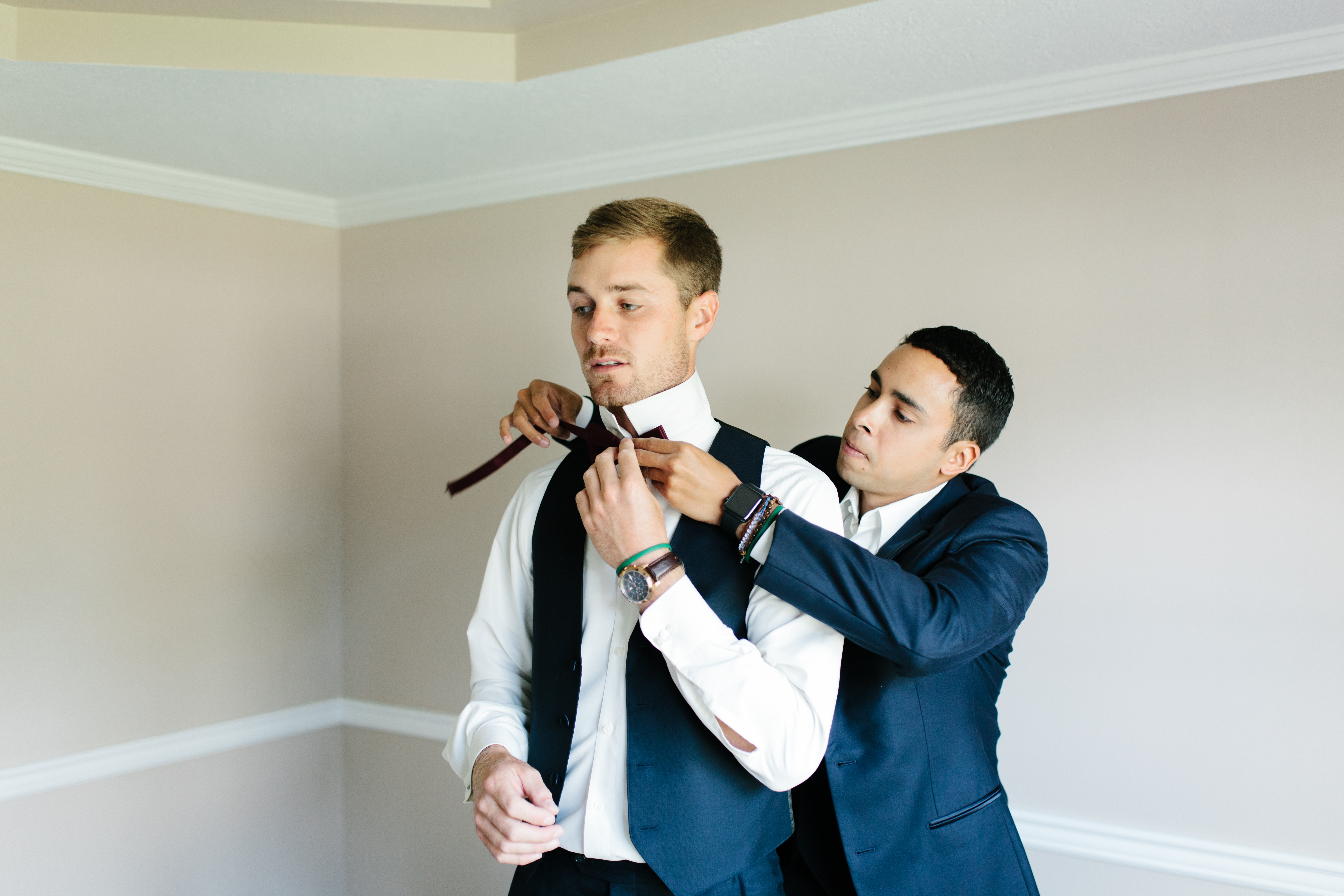 Groom puts maroon bowtie on with best man
