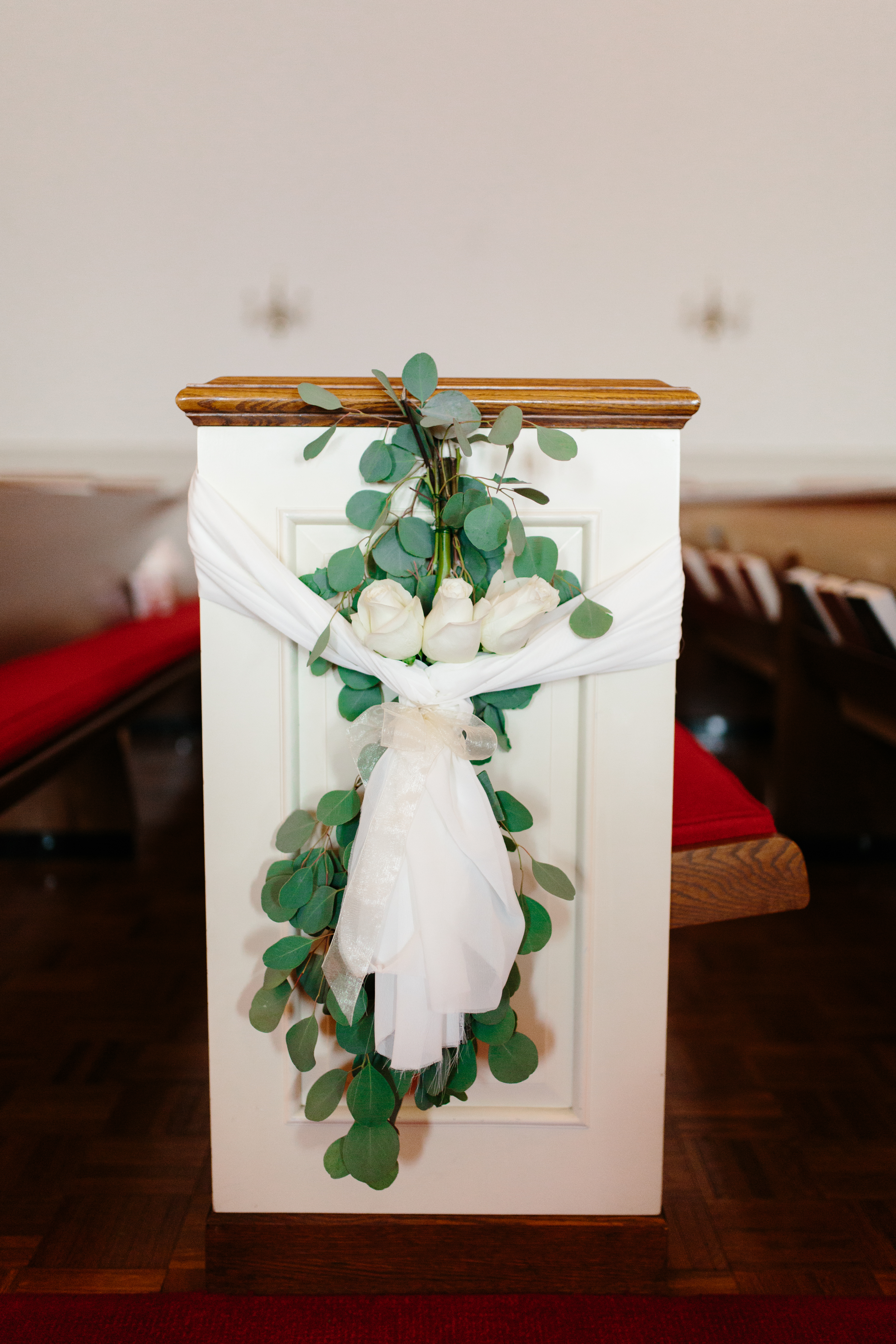 Pew decorated with white roses and silver dollar eucalyptus at wedding ceremony