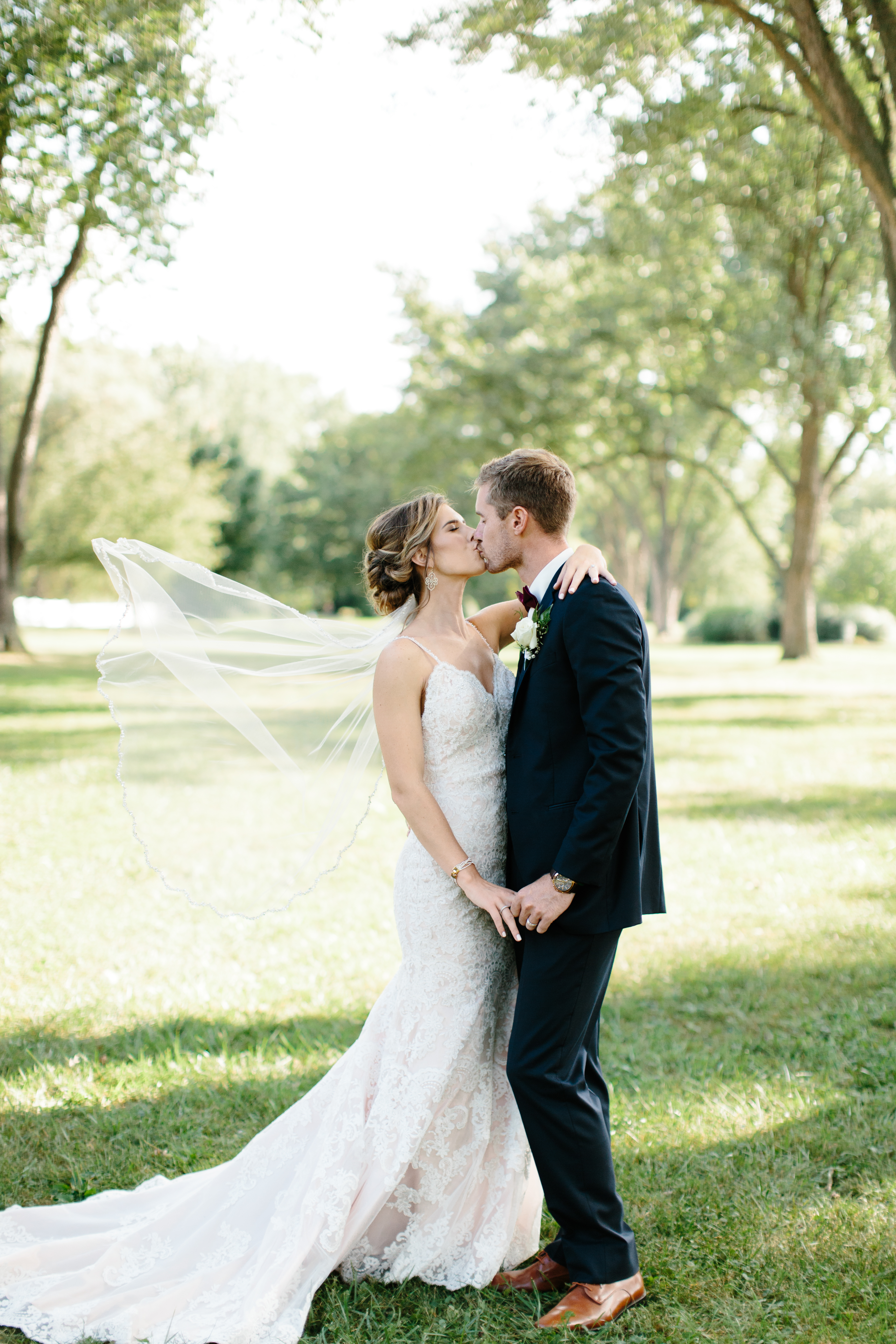 wind blows bride's veil while couple kiss
