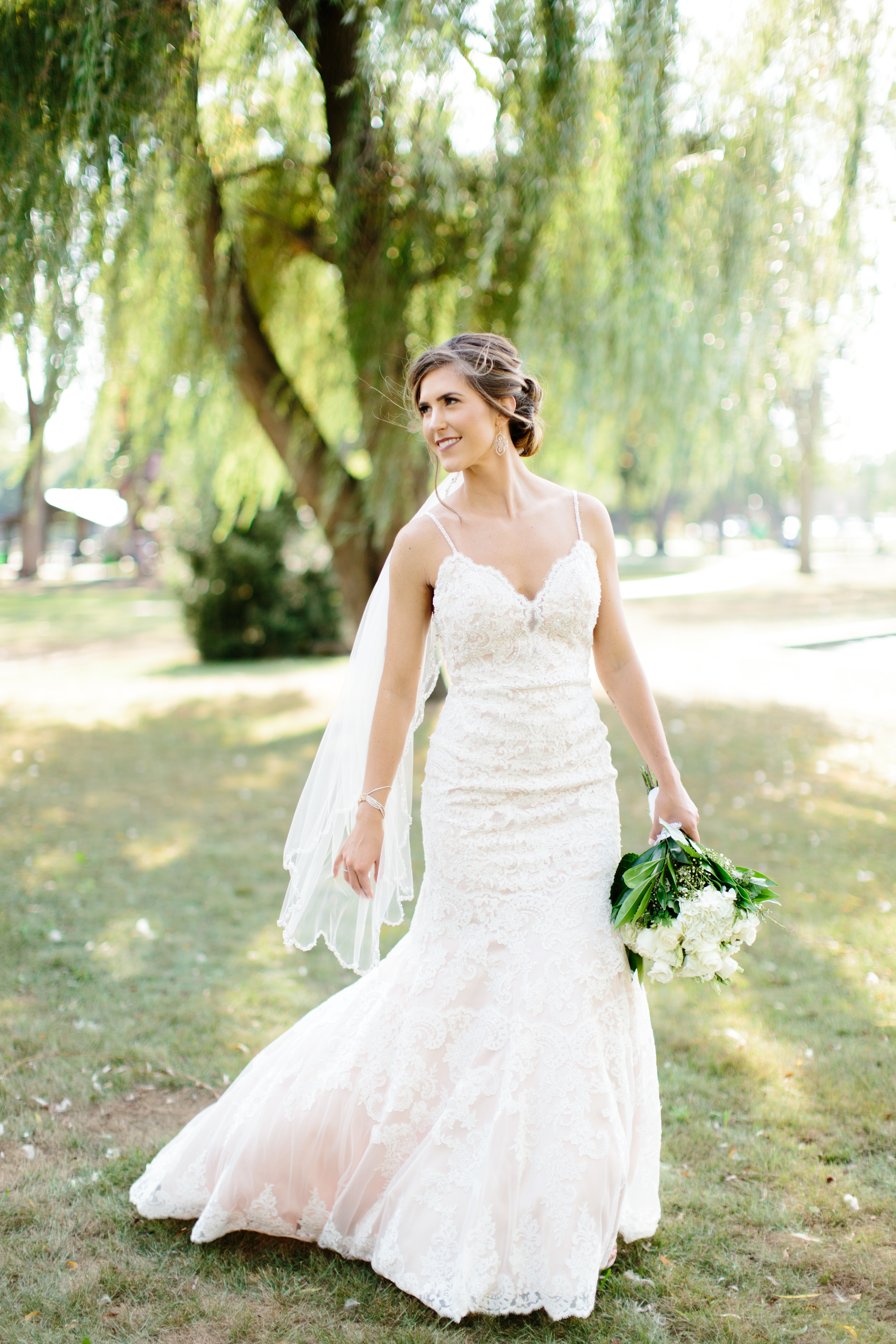 bride in blush walks under willow tree during bridal portraits