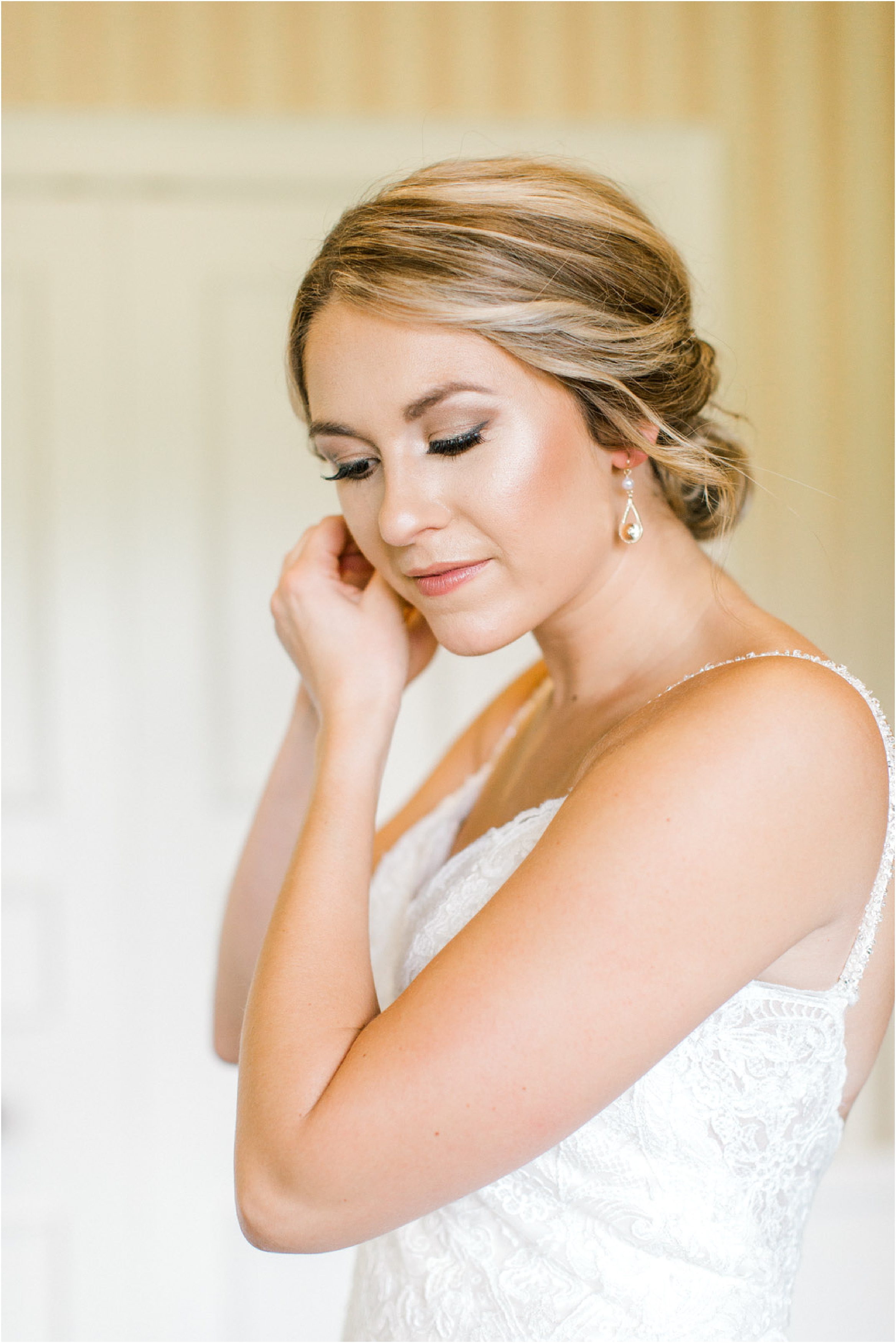 Bride putting on earrings while wearing Morilee lace gown