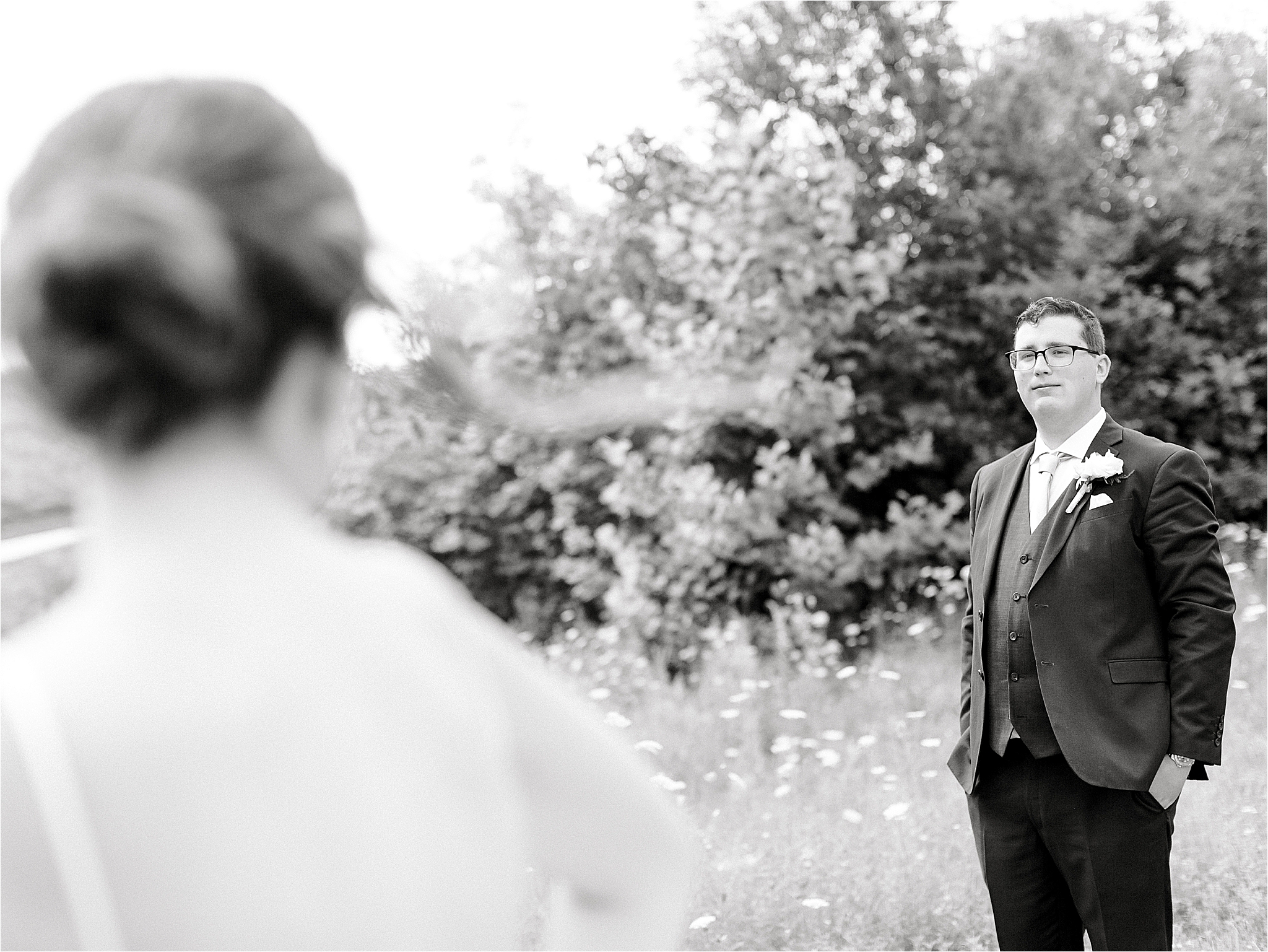 black and white image of groom looking at bride in field 